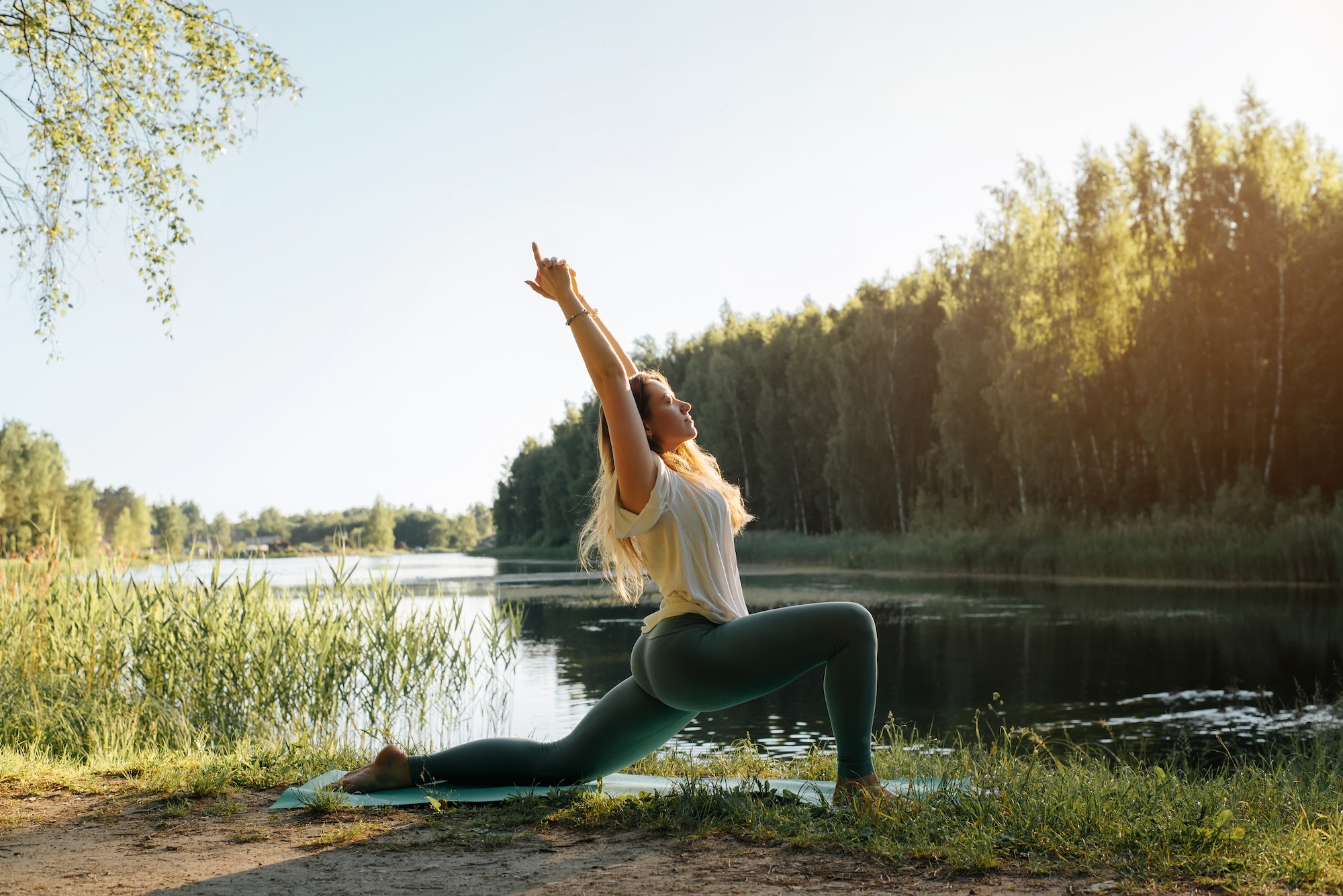 Healthy habits and wealthy outcomes yoga in nature. Young woman practicing yoga on lake at sunset, summer. Fitness model standing on